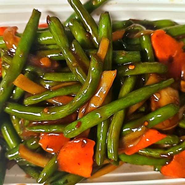 Close-up of vibrant green beans and orange carrots in a glossy brown sauce, a Chinese dish.